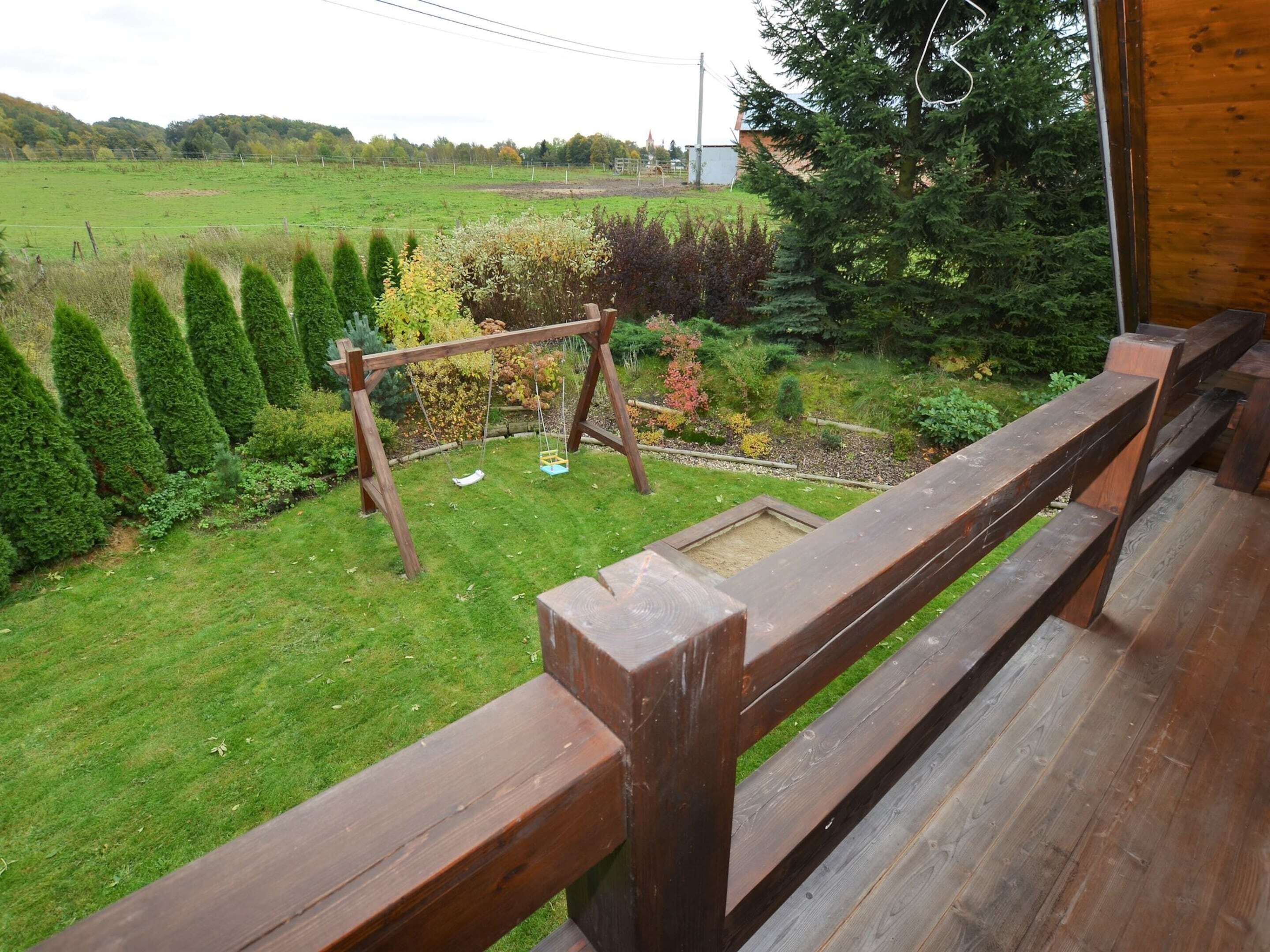Una terraza de madera con un columpio que da vista a un césped y jardín bien cuidados.