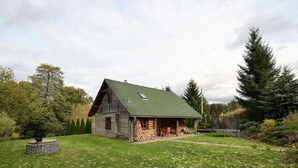 A rustic log cabin with a green roof, surrounded by a grassy yard and trees.