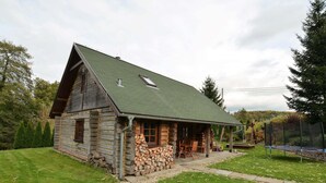 A log cabin with a green roof, a porch with outdoor seating, and a stack of firewood in front.