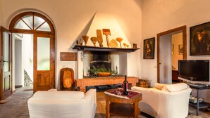 Ein geräumiges Wohnzimmer mit Kamin, weißen Sofas, einem Fernseher und einem großen Fenster.