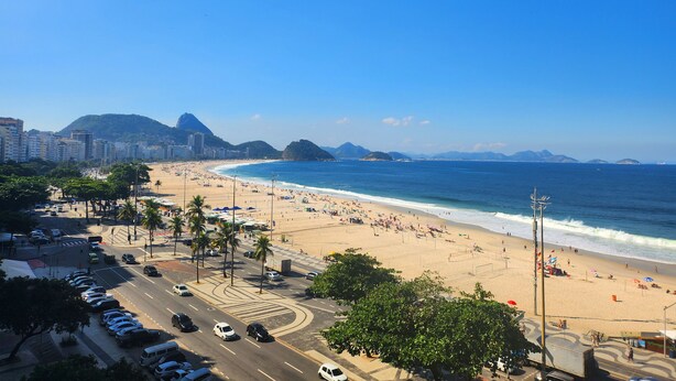 A beach with a road in the foreground and buildings in the background. - TC801 Charmoso Studio na Areia de Copacabana (Rio de Janeiro)
