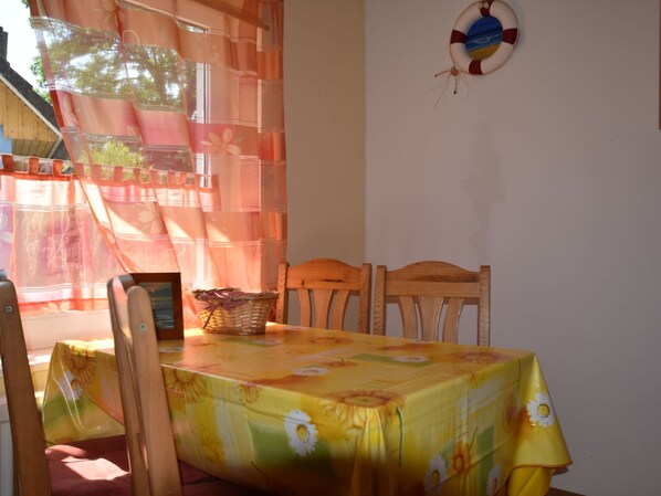 A dining area with a table covered in a floral tablecloth, wooden chairs, a basket on the table, and a life preserver hanging on the wall. - Geraeumige Ferienwohnung mit Garten (Wieck auf dem Darss)