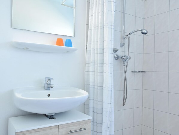 A bathroom with a white sink, a mirror, a shower, and a towel rack. - Geraeumige Ferienwohnung mit Garten (Wieck auf dem Darss)