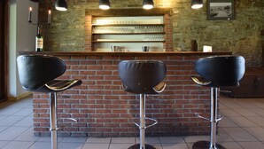 A bar area with a brick wall, three black bar stools, hanging pendant lights, and a shelf with glasses and a bottle. - Alluring Farmhouse in Lavacherie with Hot Tub (Sainte-Ode)