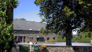 A stone building with a sloped roof, a gated entrance, and a small porch area with potted plants. - Alluring Farmhouse in Lavacherie with Hot Tub (Sainte-Ode)