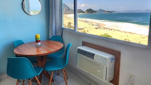 A room with a wooden table, blue chairs, a mirror, and a view of a beach with mountains. - TC802 Vistão Praia de Copa (Rio de Janeiro)