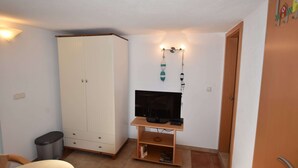 A compact room with a white wardrobe, a television on a wooden stand, a small trash bin, and a door with a handle. - Wohnung mit Terrasse im Ostseebad (Boltenhagen)