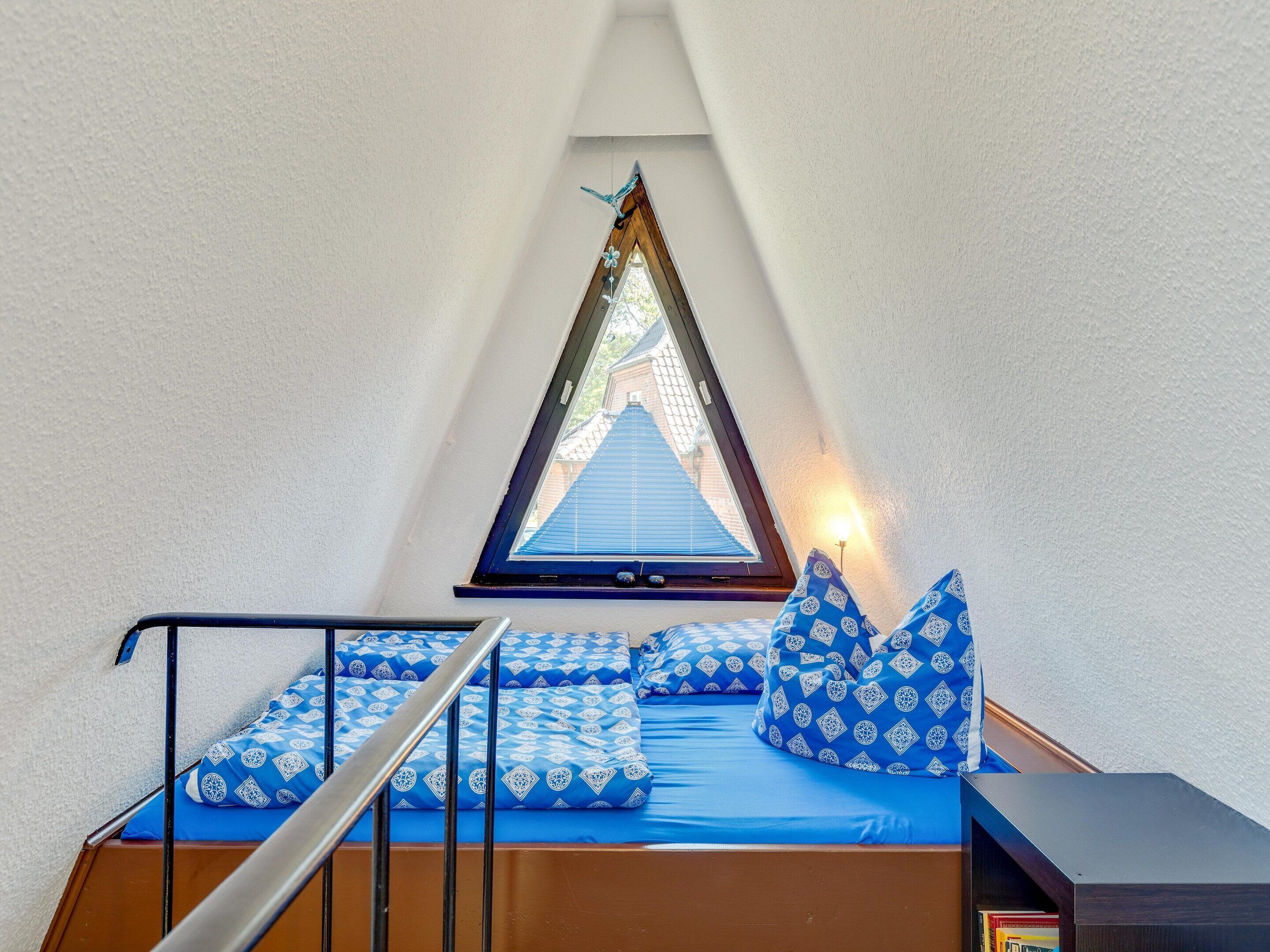 A small, triangular attic bedroom with a skylight, a bed with blue bedding, and a wooden floor.