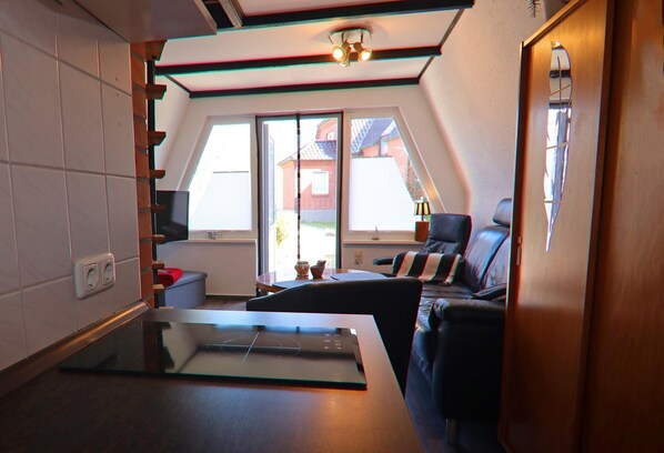 Ett modernt kök med ett bord med glasskiva, en matplats med soffa och stolar samt utsikt över ett hus genom stora fönster.