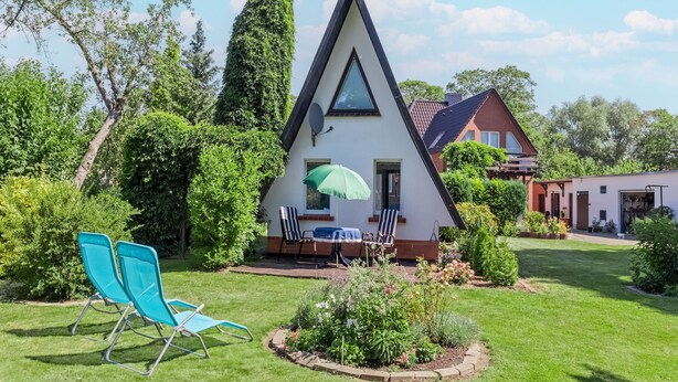 A triangular house with a satellite dish, a dining table with chairs, and a green umbrella.