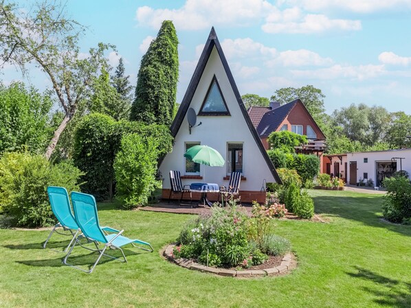 Ein dreieckiges Haus mit Satellitenschüssel, einem Esstisch mit Stühlen und einem grünen Sonnenschirm.
