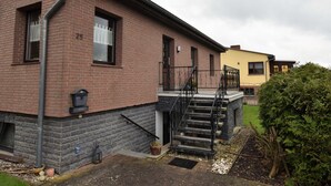 Ein Backsteinhaus mit einer Treppe, die zu einer Veranda führt, einem Briefkasten und einem kleinen Garten.