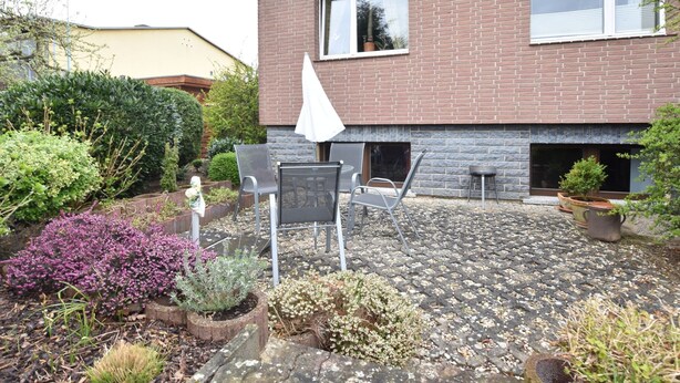 Ein Backsteinhaus mit einer Terrassenanlage, die Gartenmöbel und Pflanzkübel beinhaltet.