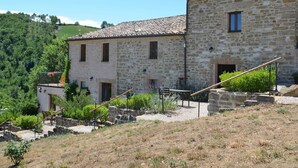 A stone building with a tiled roof, a small balcony with plants, and a gravel pathway leading to a wooden bench. - Belvilla by OYO Sole e Luna (Pergola)