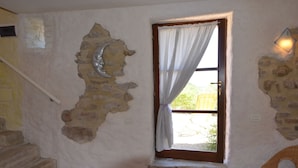 A room with a stone wall, a wooden door with a white curtain, a wicker chair, and a staircase. - Belvilla by OYO Sole e Luna (Pergola)