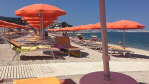 A beach with rows of sun loungers and orange umbrellas, a clear blue sky, and a calm sea. - Belvilla by OYO Sole e Luna (Pergola)