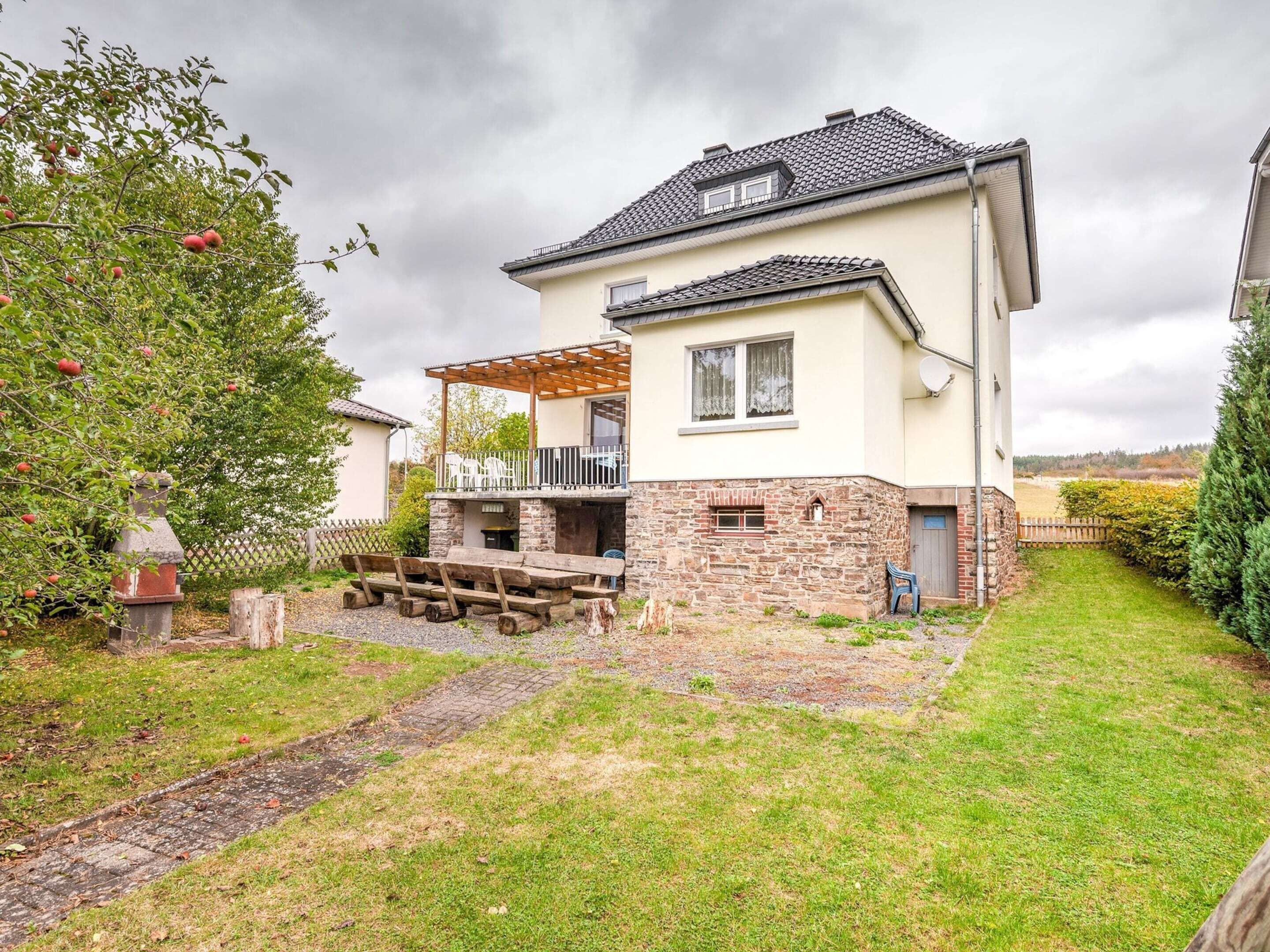 A two-story house with a stone facade, a covered patio, and a garden.