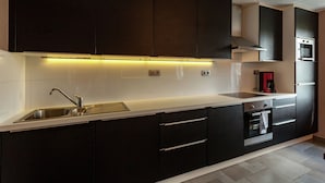 A modern kitchen with dark cabinetry, a stainless steel sink, and a built-in oven. - Le Bizet Vacation Home (Comines-Warneton)