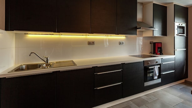 Una cocina moderna con armarios oscuros, un lavamanos de acero inoxidable y un horno empotrado.