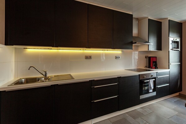 A modern kitchen with dark cabinetry, a stainless steel sink, and a built-in oven.