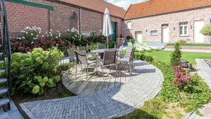 A patio with outdoor furniture, a brick building, and a green lawn. - Le Bizet Vacation Home (Comines-Warneton)