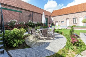 A patio with outdoor furniture, a brick building, and a green lawn. - Le Bizet Vacation Home (Comines-Warneton)
