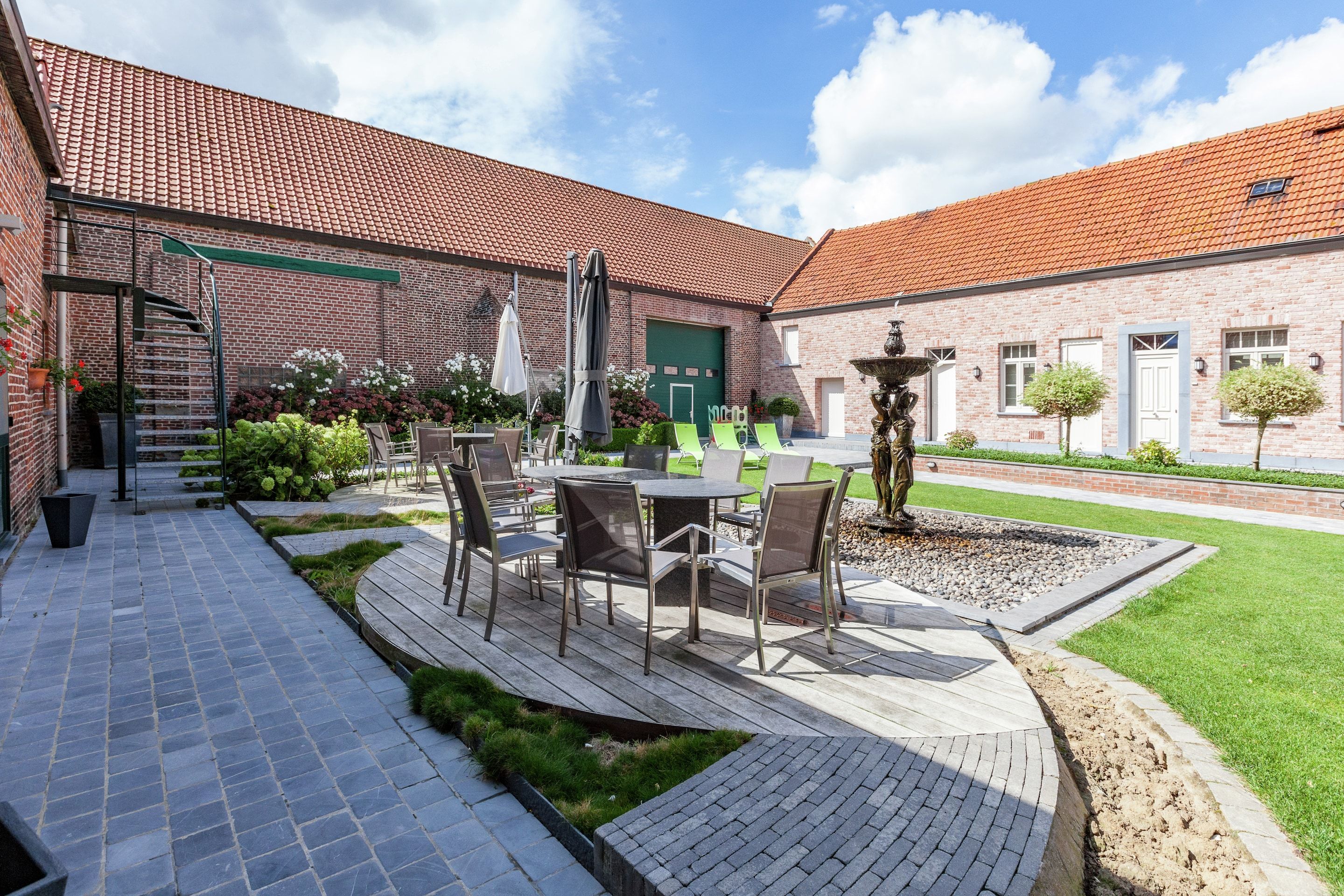 A courtyard with a brick building, outdoor seating, a staircase, and a fountain.