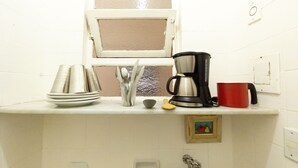 Une cuisine avec une fenêtre, une machine à café, une tasse rouge et une pile d’assiettes.