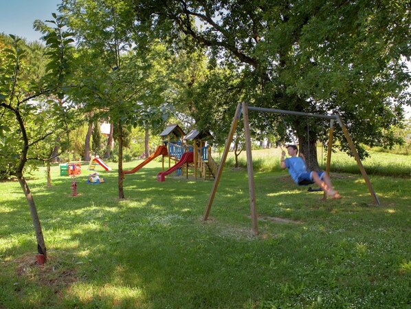 A playground with swings and slides, surrounded by trees and grass.