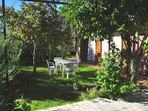 A garden with a table and chairs, surrounded by trees and a building.