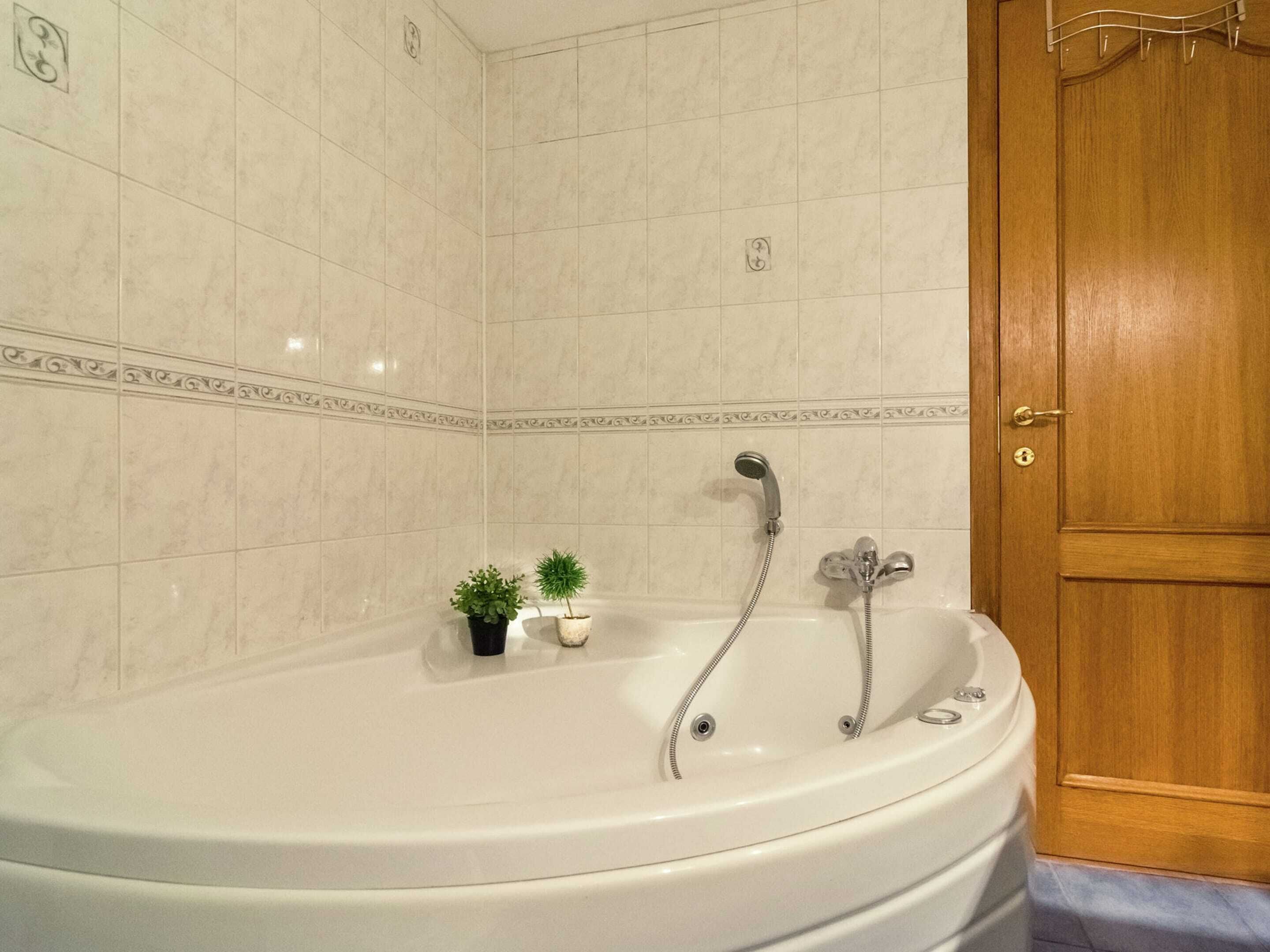 A bathroom with a white bathtub, a wooden door, and a small potted plant on the floor.