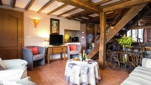 A cozy living room with a wooden ceiling, a television, a table with a floral tablecloth, and a staircase with a vintage wheelbarrow. - Scenic Retreat in Gimnee (Doische)