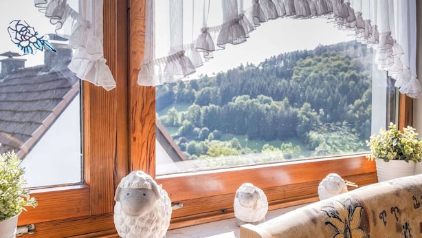A window with a view of a forest, a wooden window frame, and two white sheep figurines on a windowsill. - Large Holiday Apartment near Willingen with Private Garden & Terrace (Medebach)