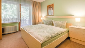 A bedroom with a bed, two bedside tables, a radiator, and a window with curtains. - Large Holiday Apartment near Willingen with Private Garden & Terrace (Medebach)
