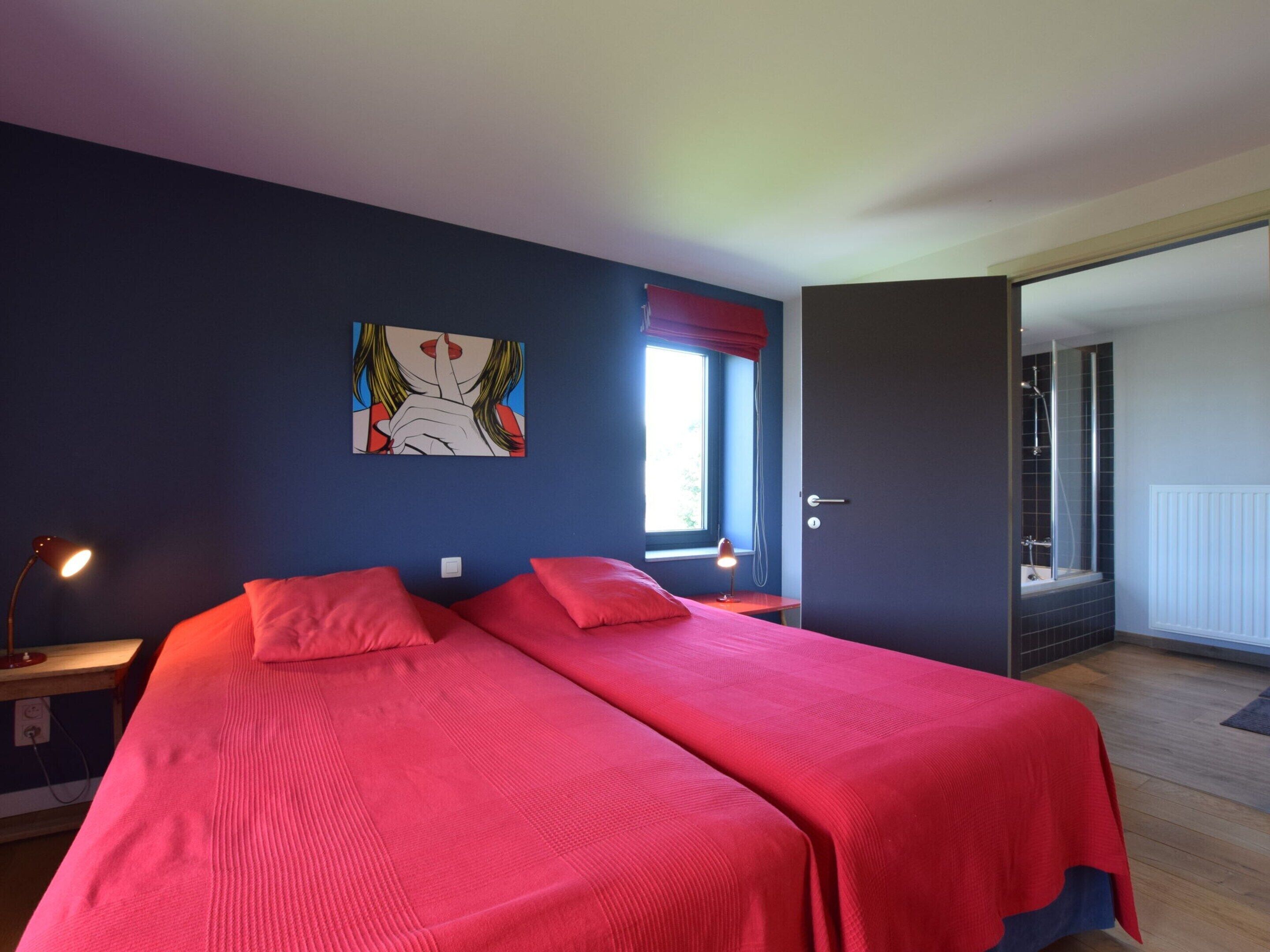 A bedroom with two beds, a window with red curtains, a door leading to a bathroom, and a painting on the wall.