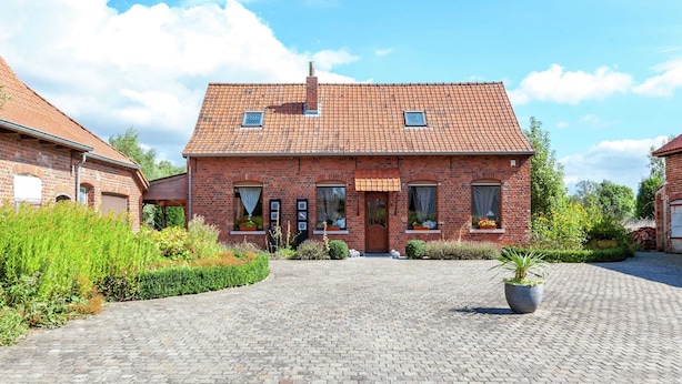 Een gebouw van baksteen met een pannendak, een centrale ingang en een geplaveid binnenterrein.