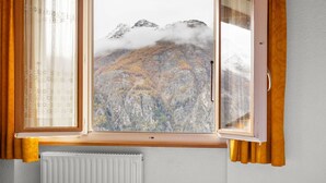 Ett sovrum med utsikt över ett bergigt landskap genom ett fönster med träpersienner.