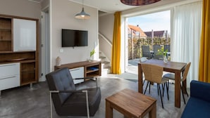 Ein modernes Wohnzimmer mit einer Couch, einem Couchtisch, einem an der Wand montierten Fernseher und einem Essbereich mit Tisch und Stühlen.