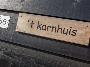 Een houten bord met de tekst 't Karnhuis' bevestigd aan een donker houten oppervlak.