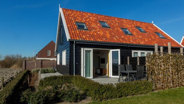 Ein modernes Haus mit Satteldach, großen Fenstern und einer Terrasse mit Gartenmöbeln.