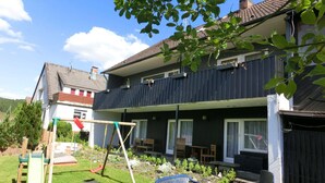 A two-story house with a balcony, a swing set, and a patio area with a table and chairs. - Apartment With Meadow View in Wildemann (Clausthal-Zellerfeld)