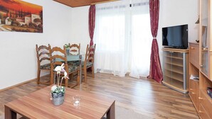 A cozy living room with wooden flooring, a dining table with chairs, a TV on a stand, and a painting on the wall. - Apartment With Meadow View in Wildemann (Clausthal-Zellerfeld)