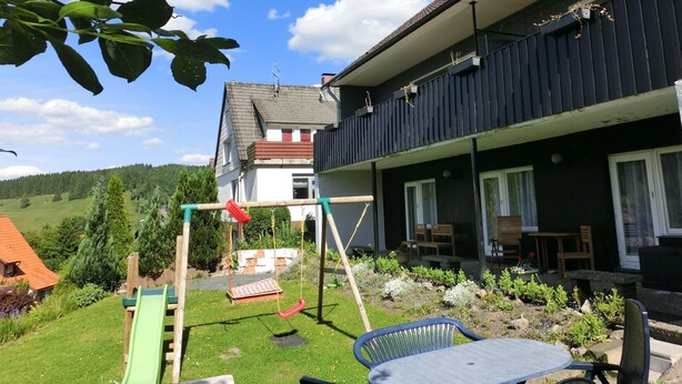 A residential backyard with a swing set, a green slide, a patio table, and a garden with various plants and a small pond. - Apartment With Meadow View in Wildemann (Clausthal-Zellerfeld)