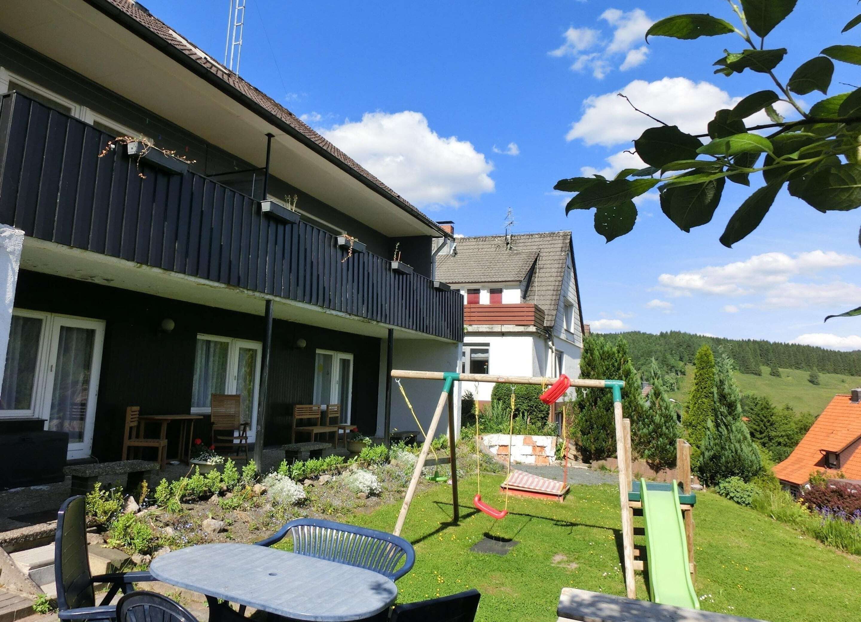 A residential property with a balcony, outdoor seating, a swing set, and a garden.