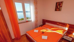 Une chambre d’hôtel avec un lit en bois, une literie orange, une fenêtre donnant sur l’eau et une petite table sur laquelle est posé un vase.