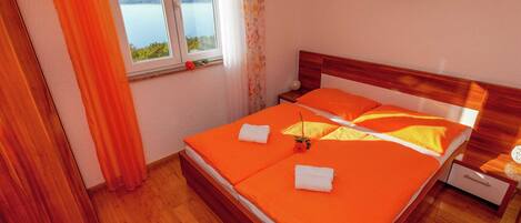 A hotel room with a wooden bed, orange bedding, a window with a view of the water, and a small table with a vase.