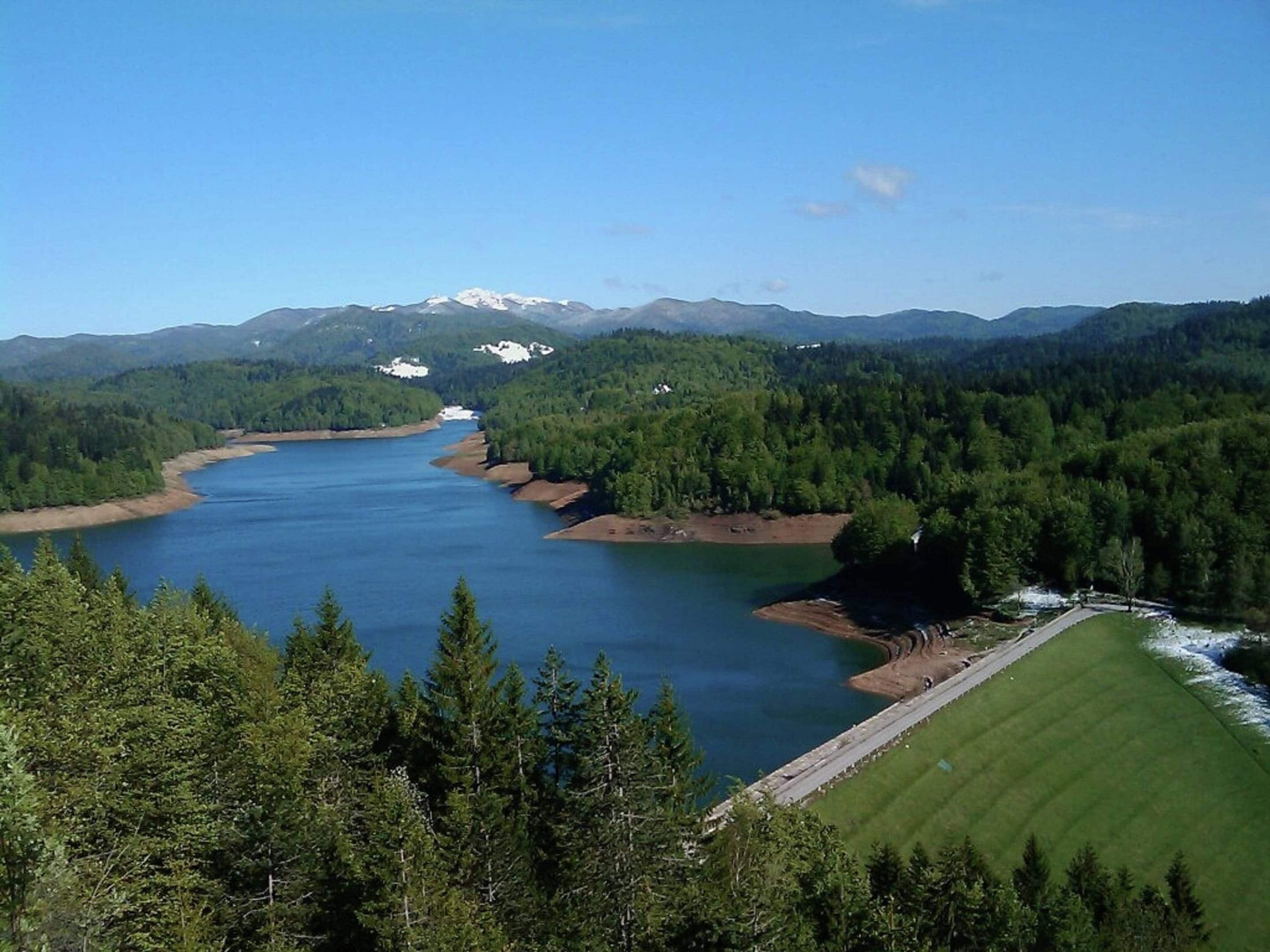 Une rivière serpentant à travers une vallée boisée, avec un pont et une vue sur des montagnes lointaines.