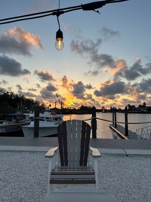 Une jetée avec une chaise donnant sur un coucher de soleil sur l’eau, des bateaux et un quai.