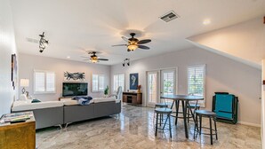 A spacious living room with a large gray sofa, a flat-screen TV, and a dining area with a table and chairs.