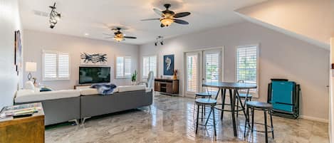 A spacious living room with a large gray sofa, a flat-screen TV, and a dining area with a table and chairs.